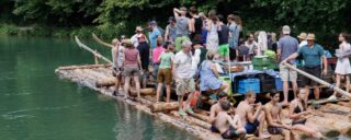 Passeio de balsa no rio Isar. A imagem mostra uma balsa de madeira navegando no rio, com um grupo de pessoas sobre ela.